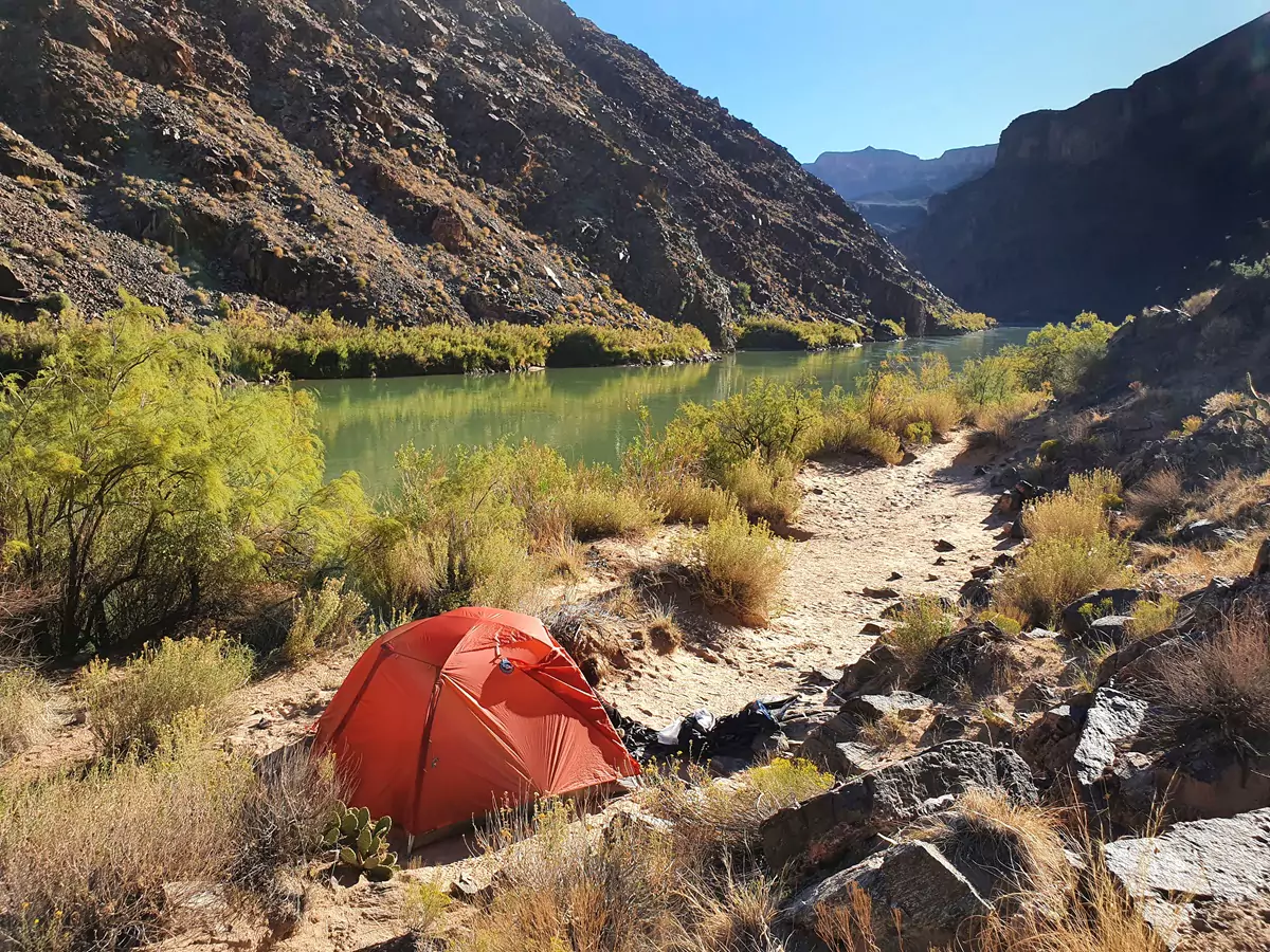 An orange tent set up for backcountry camping by the Colorado River at Hermit Rapids, Grand Canyon.