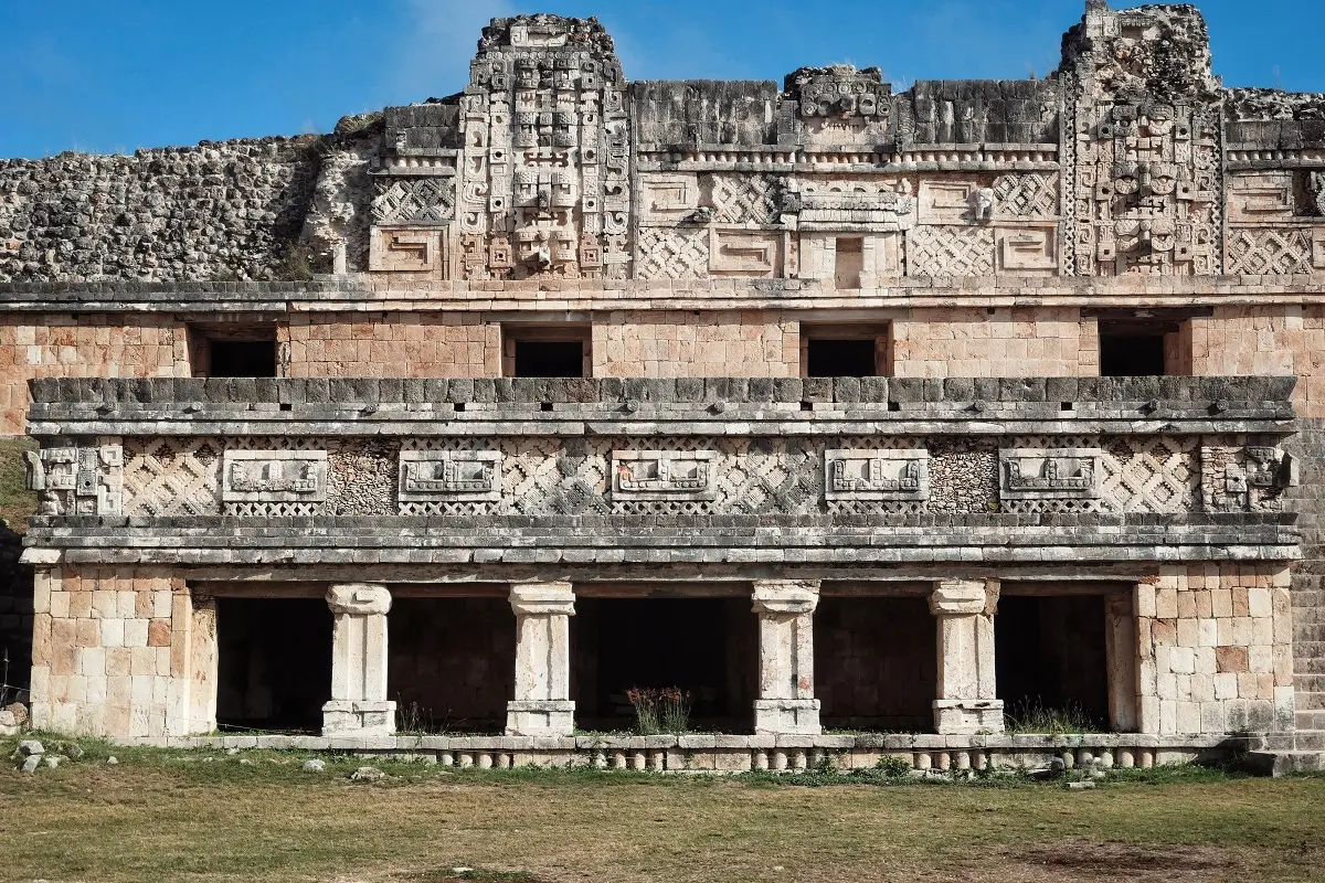 Ornate architectural style on display at the Mayan ruins of Uxmal, featuring columns, stone faces, carvings and tile like mosaic patterns.