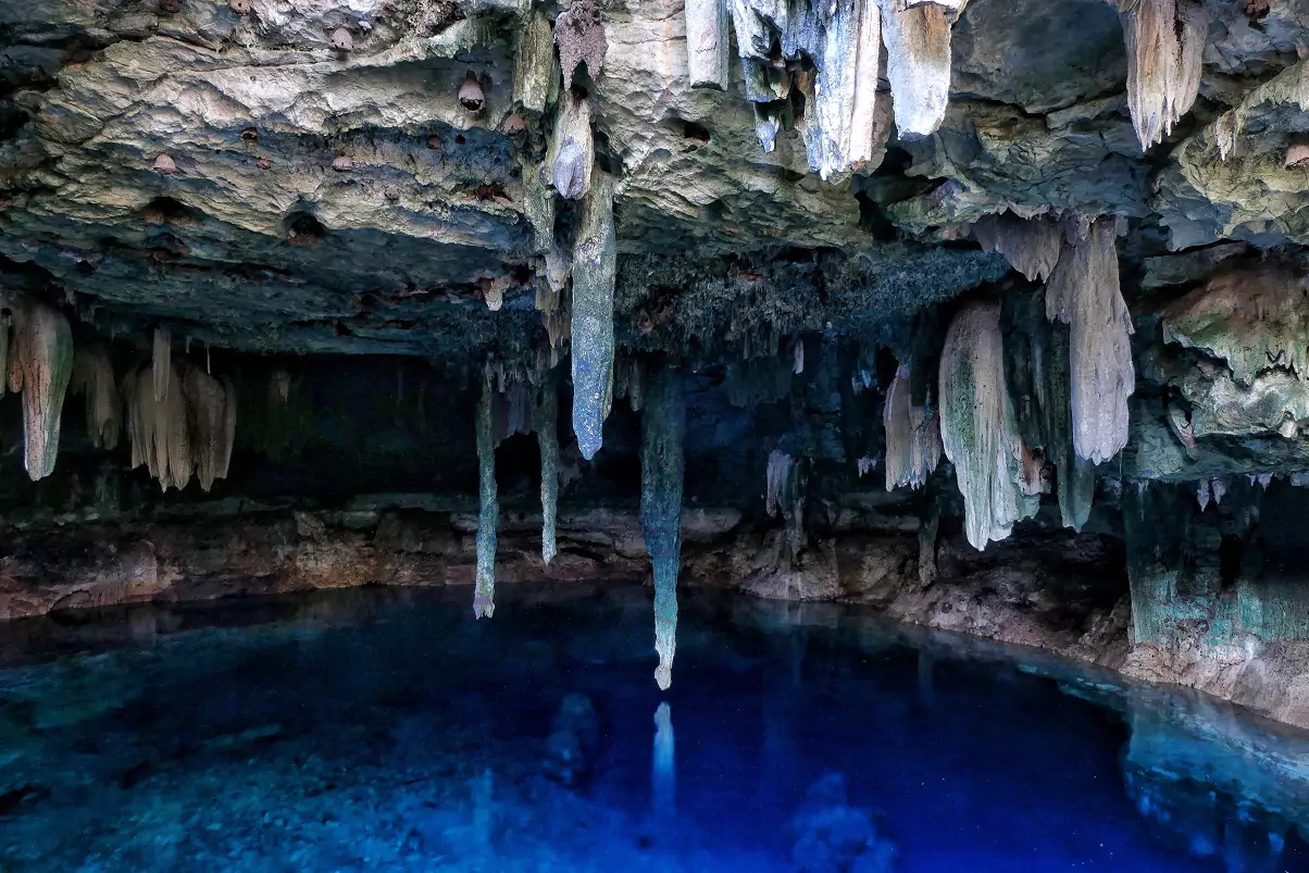 Kankirixche cenote south of Merida with stalactice formations growing down towards the deep blue, clear waters inside the pool below.
