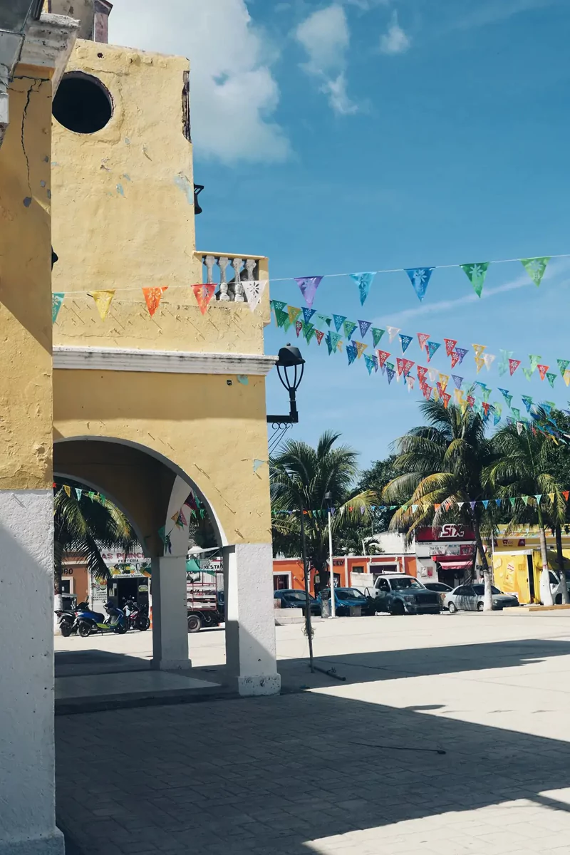 The town square in Celestun with colourful bunting attached to a yellow building, leading off in multiple directions.