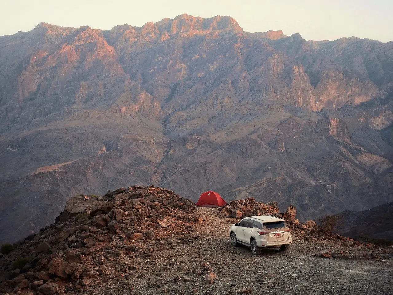 A dust covered four-wheel drive vehicle parked near a red tent at a campsite in Oman's Wadi Bani Kharus.