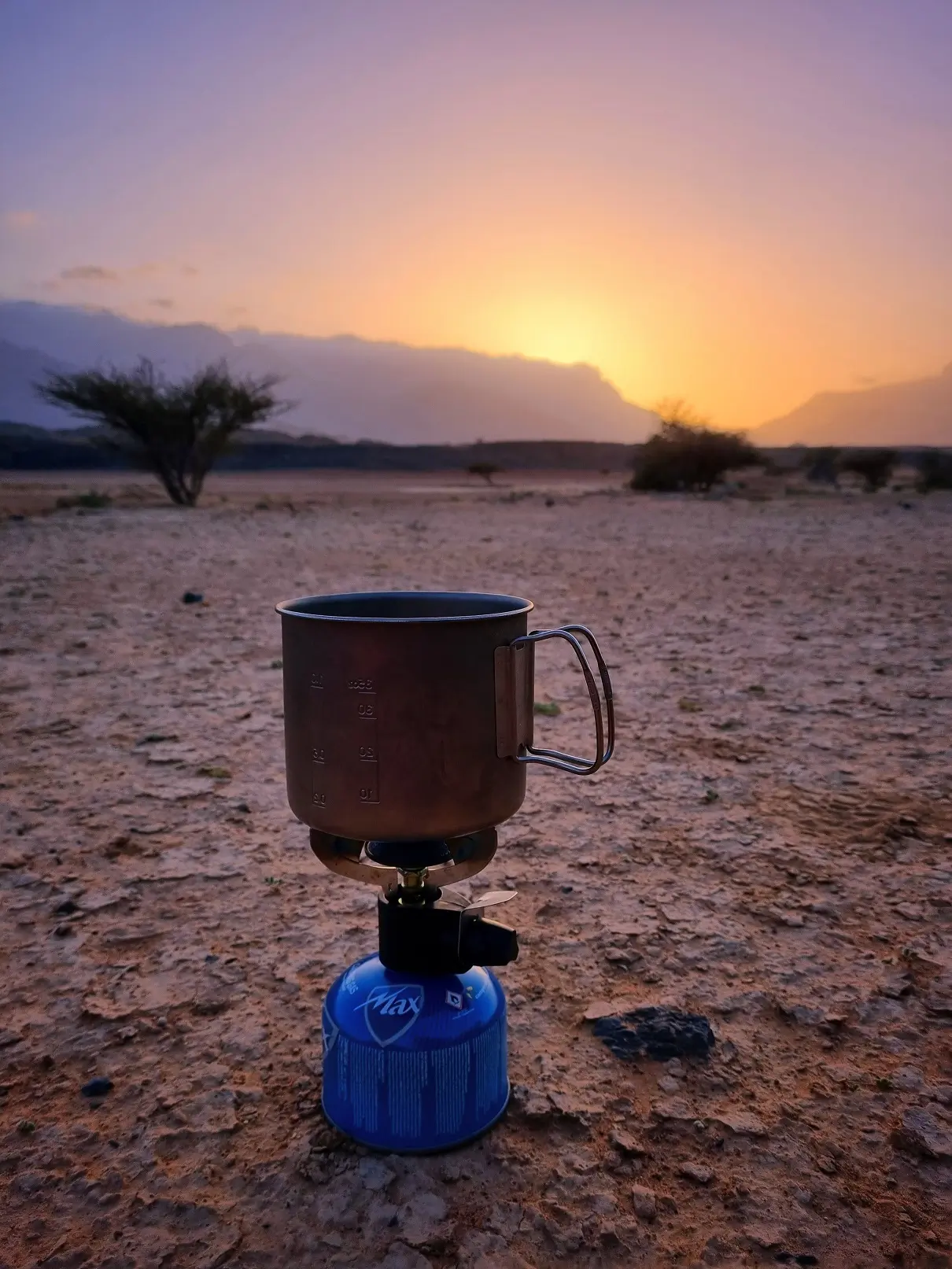 A lit butane cannister heating a pot of water at an Oman campsite at sunset in Wadi Dayqah.