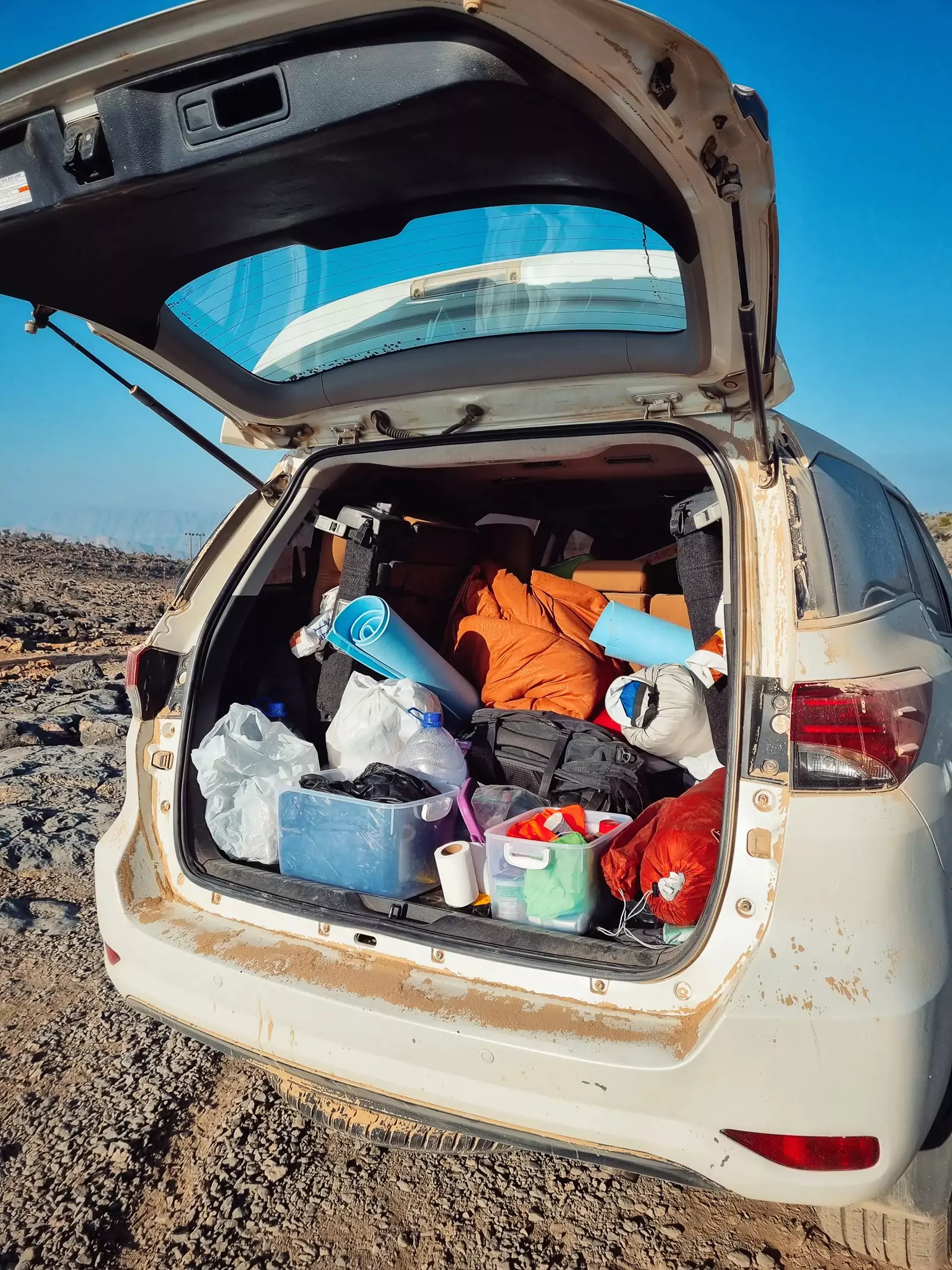 The boot of a white, offroad 4X4 vehicle completely full of various camping gear provisions.