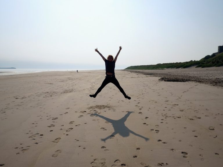 Jumping on the beach on the Northumberland Coast with a Castle in the far background