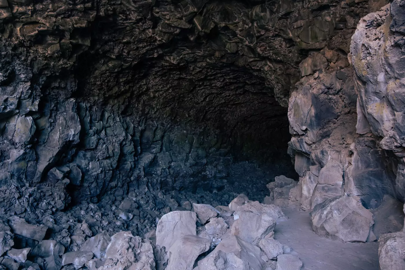 Uneven rocky entrance leading into the darkness of a lava tunnel at Lassen.