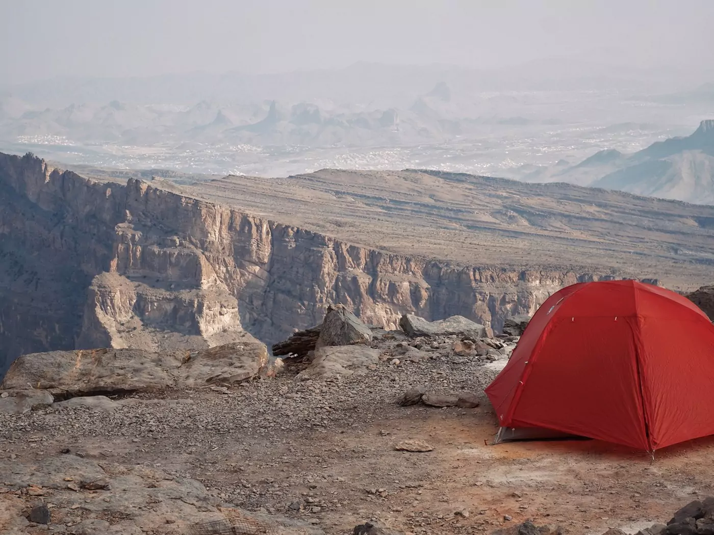 An orange tent set up by a cliff edge on Jebel Shams at sunset with long reaching views behind.