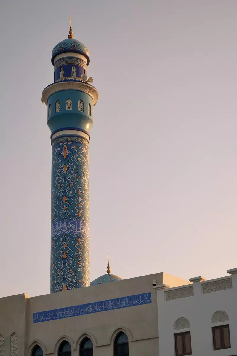 The minaret of an ornately patterned mosque at the Mutrah corniche in Muscat at sunset.