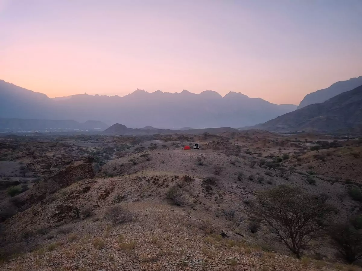 A white car and an orange tent at a campsite overlooking Jebel Shams.