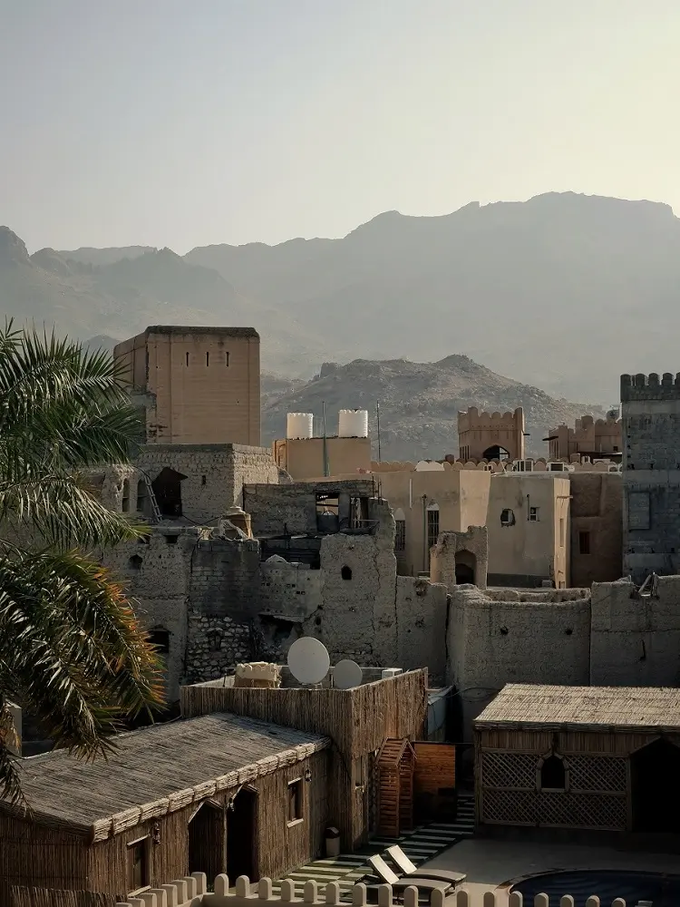 View of Old Nizwa town and its ruined buildings with a hazy mountain backdrop.