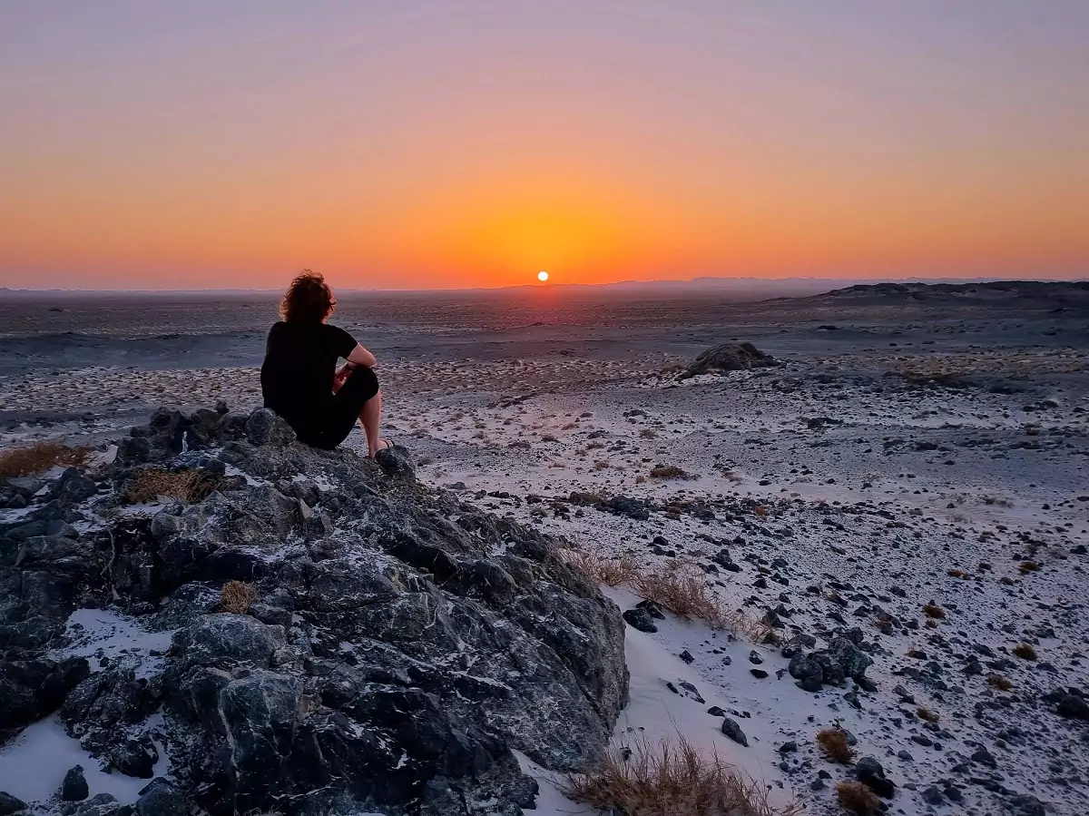 A person sat on a rock, looking at the sun rising in the distance on Masirah Island.