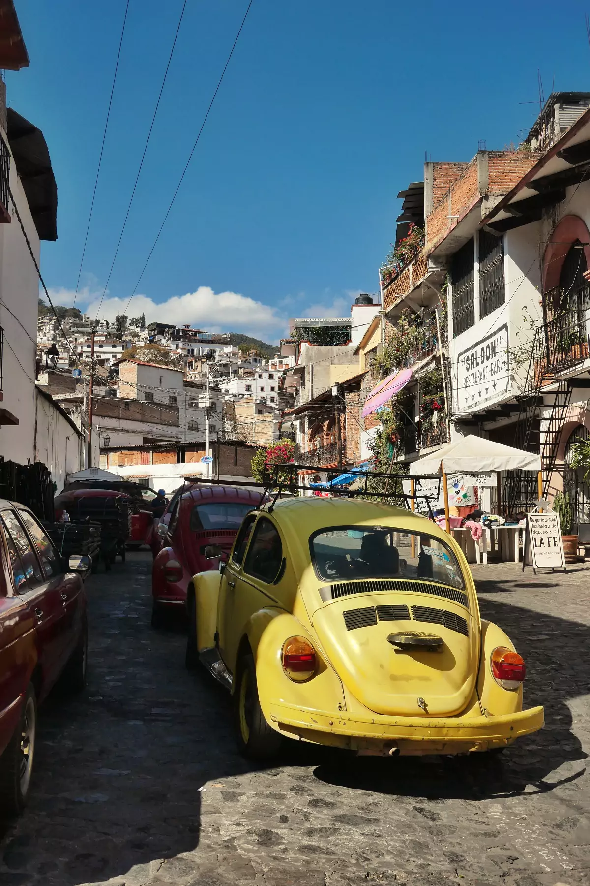 A red and a yellow VW Beetle double parked on the cobblestone roads of Taxco, Mexico.