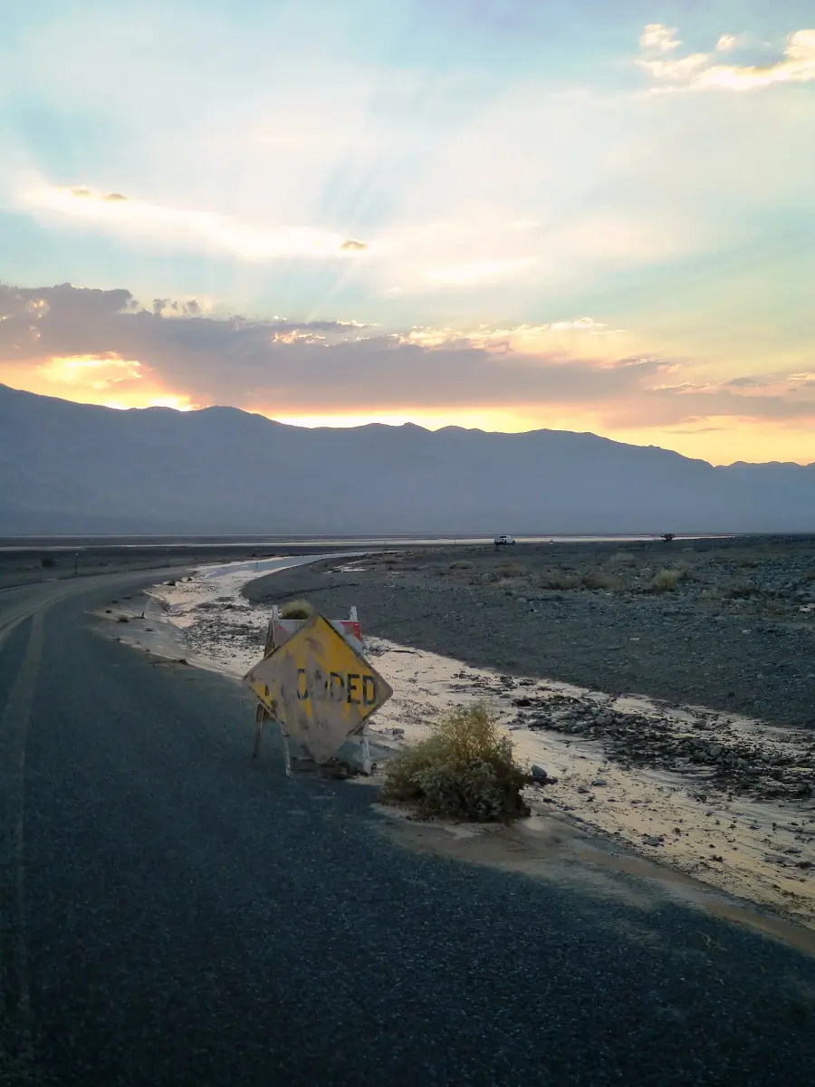 A partially obscured sign warning the road is flooded as the sun rises from behind a mountain in the distance in Death Valley.
