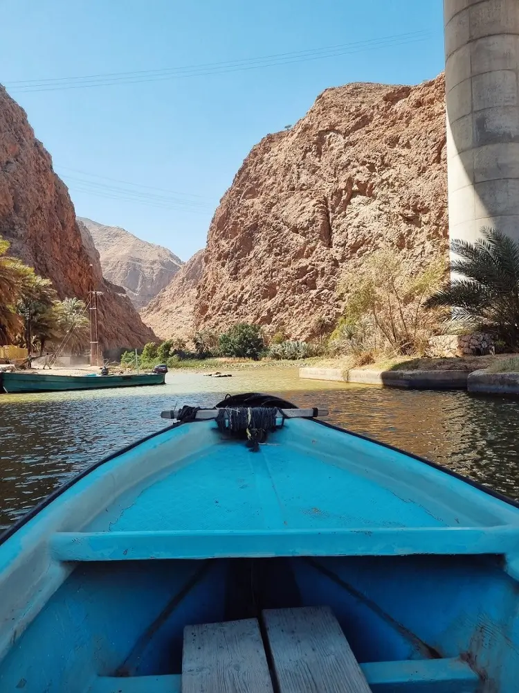 A blue boat on the water heading towards the start of the Wadi Shab hike