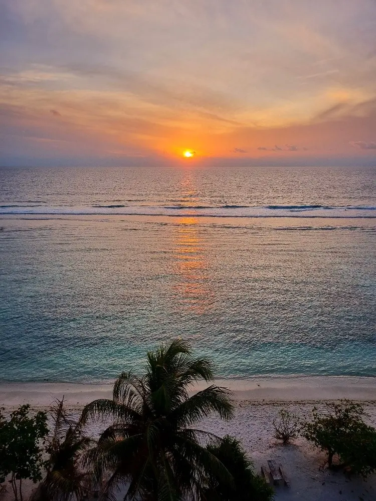 An orange sunrise over the clear blue waters by the sandy shores of Hulhumalé, the Maldives.