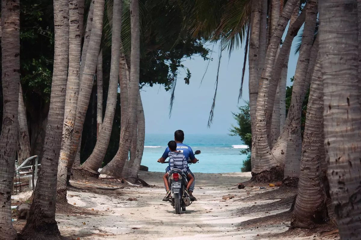 A parent and child riding along the street on a motorbike in Thoddoo.