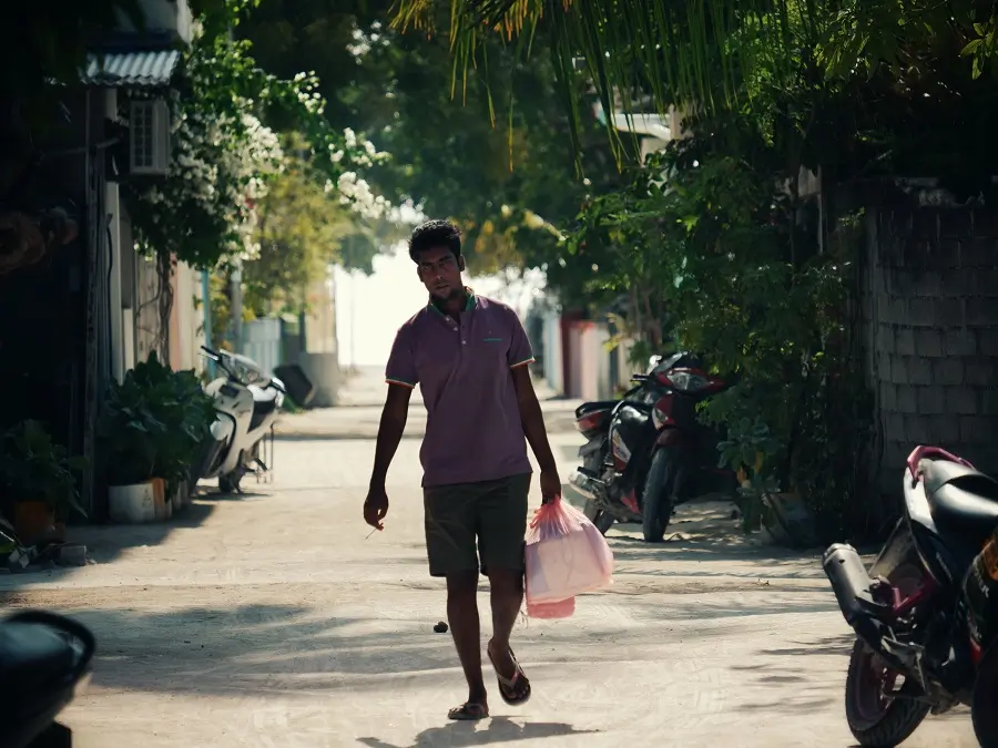 A person walking with their shopping along a street in Maafushi in the Maldives.