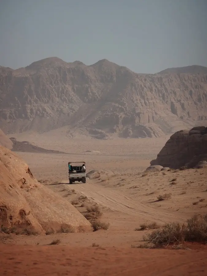 A white Toyota van driving along a sandy path through Jordan's Wadi Rum.