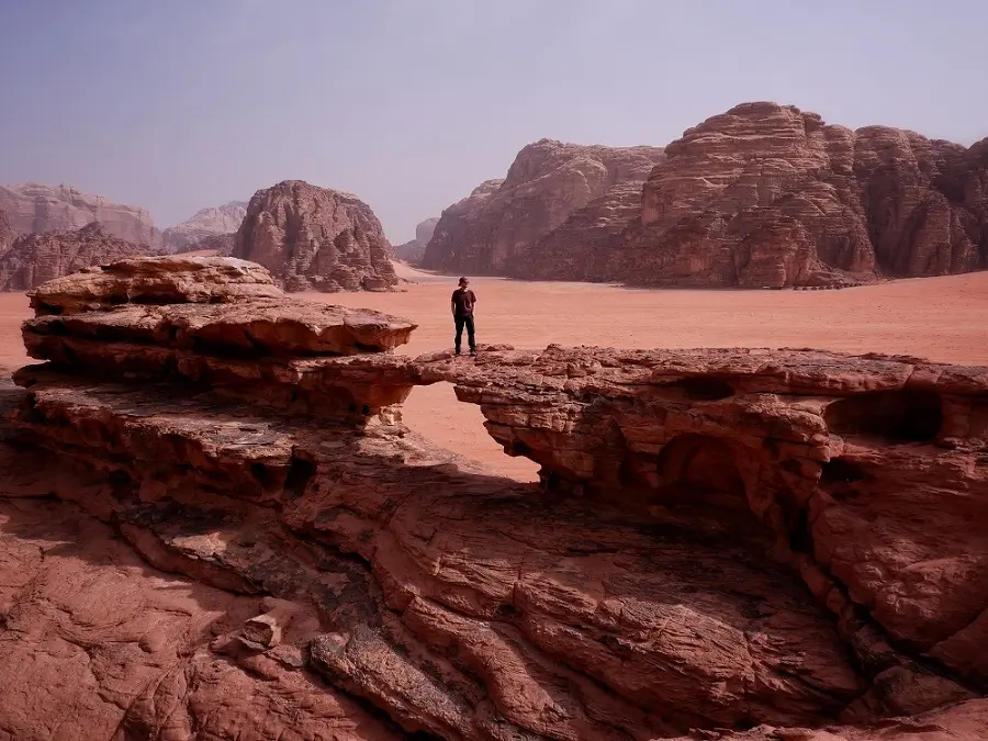 A person standing on Little Rock Bridge, one of the regular stops of most Wadi Rum Jeep Tours.