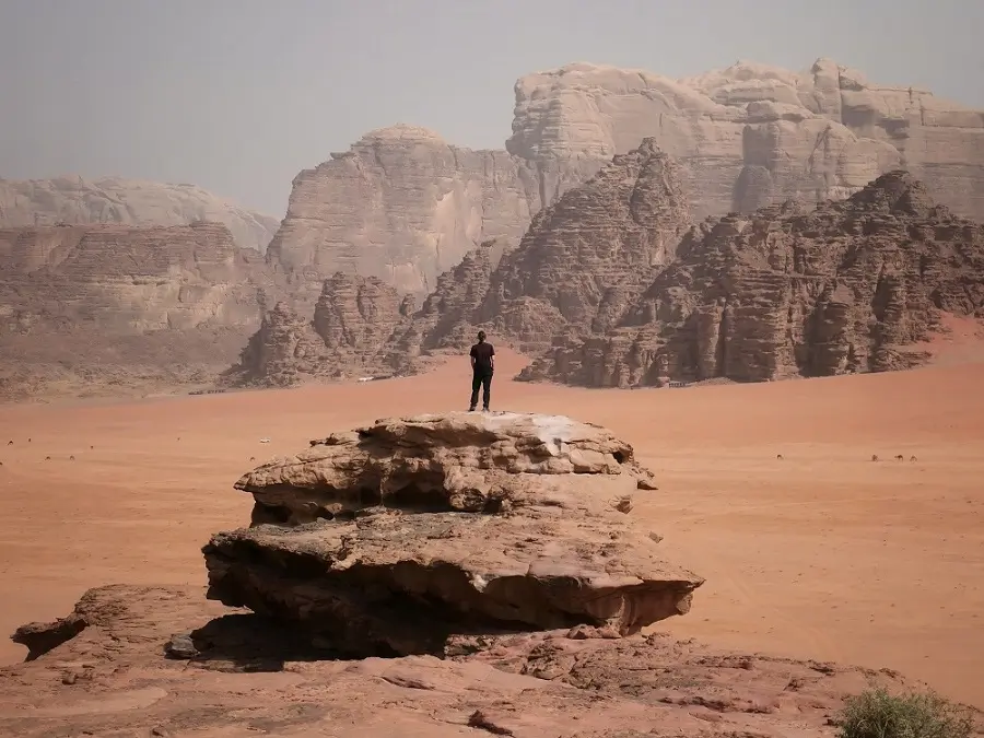 A person stood atop a rocky outcrop in Wadi Rum at Little Rock Bridge.