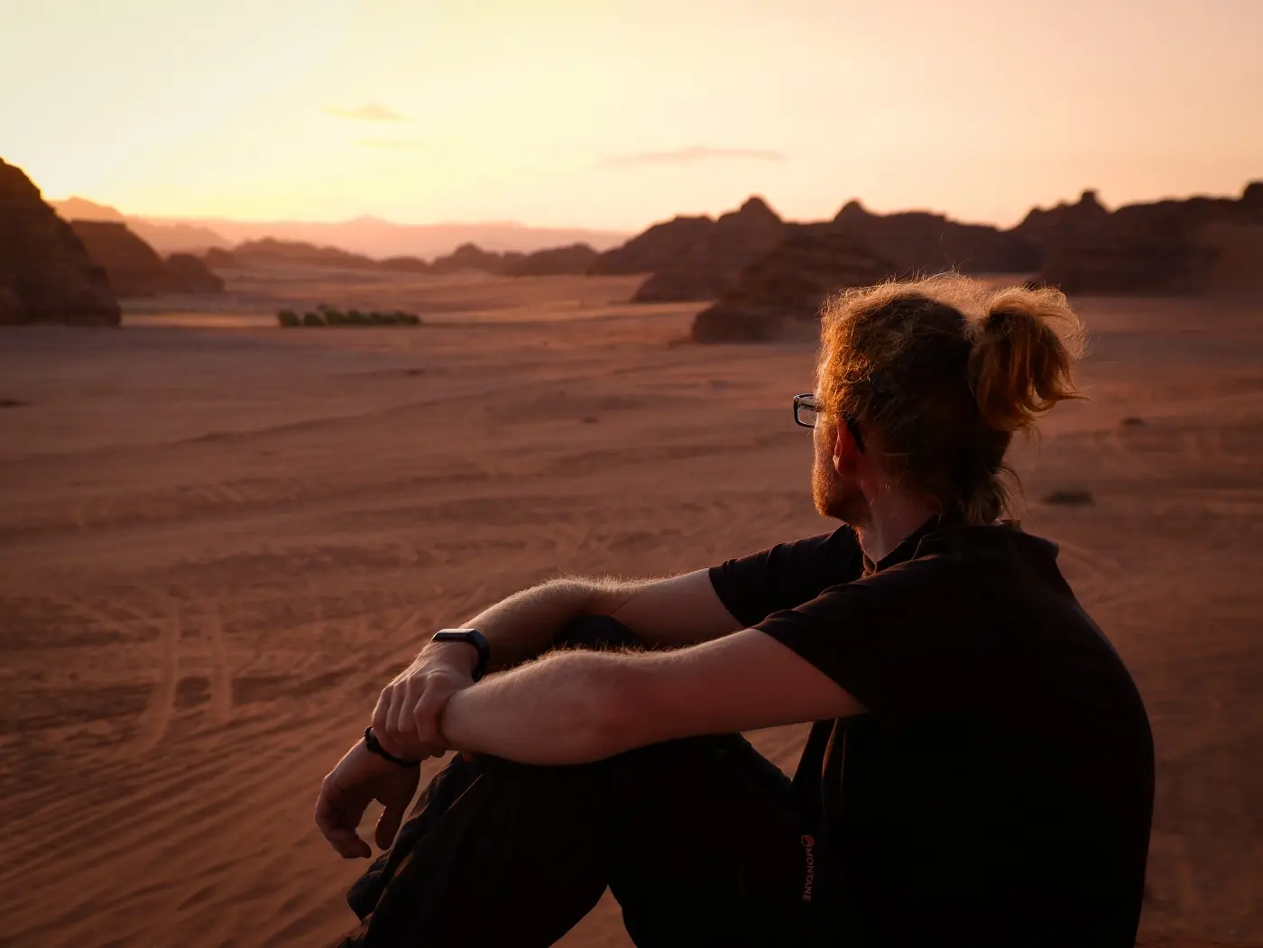 A person sitting in the sandy, desert landscape around Al-Ula, Saudi Arabia.