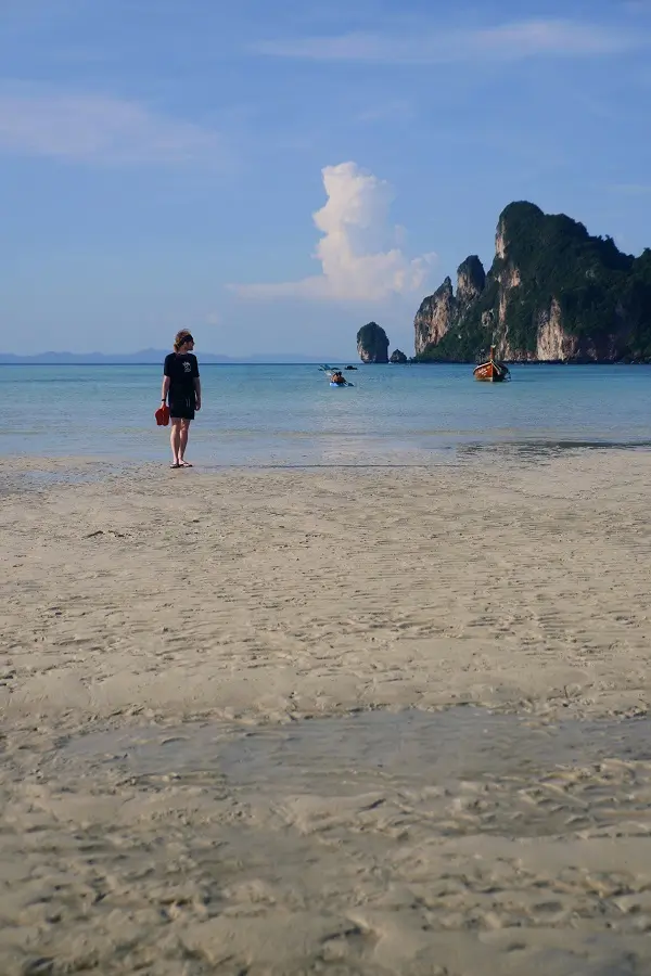 A person standing on the beach at Ko Phi Phi Don, holding flip-flops.