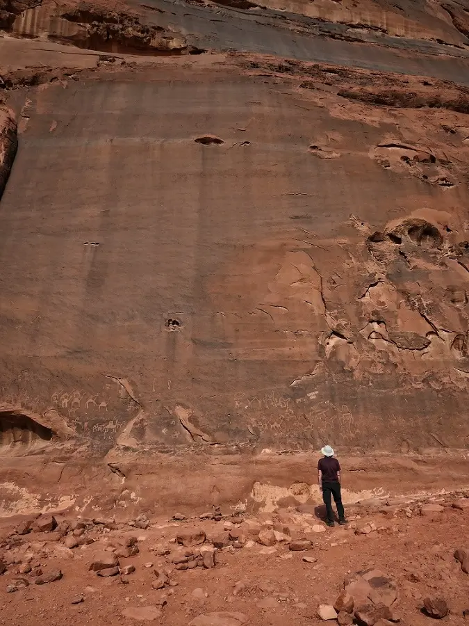 A man wearing a white hat looking at Petroglyphs on a rock wall in Wadi Rum, Jordan.