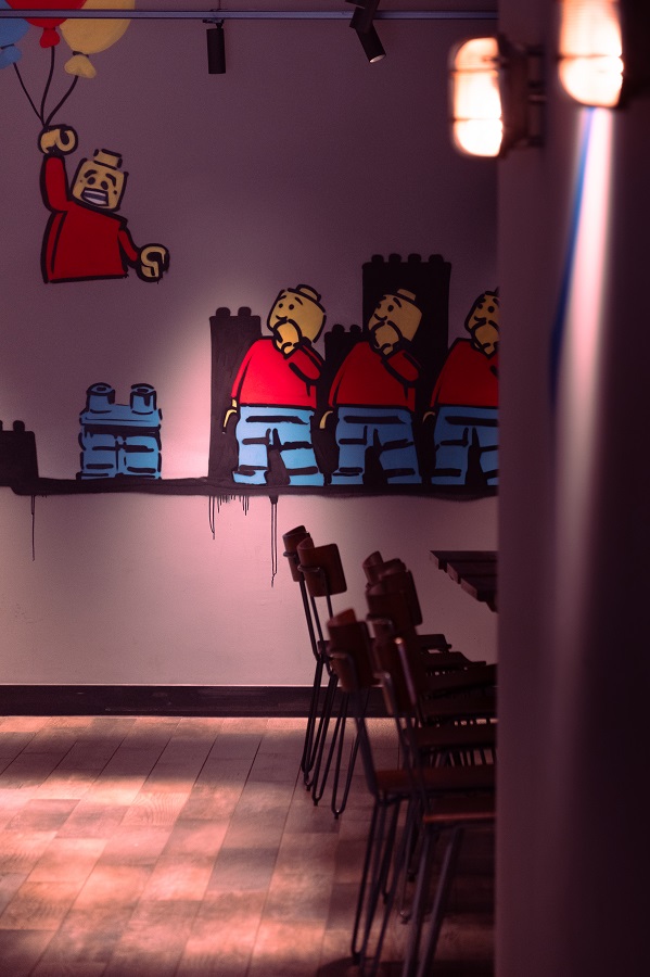 Humorous wall art depicting a Lego man becoming detached from their legs, painted on a wall in a café in Leeds.