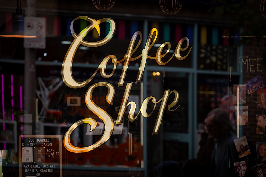 Colourful golden hued cursive writing on the window of a coffee shop saying 'Coffee Shop'.