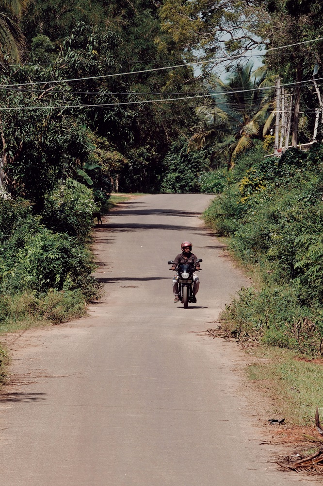 A motorcycle rider wearing a helmet, driving along the road in Sri Lanka.