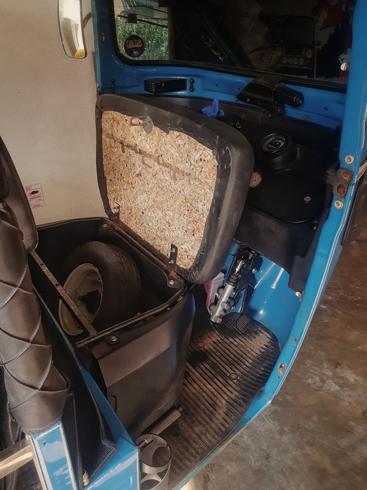A spare wheel under the open driver's seat in a blue Sri Lanka rental tuktuk.
