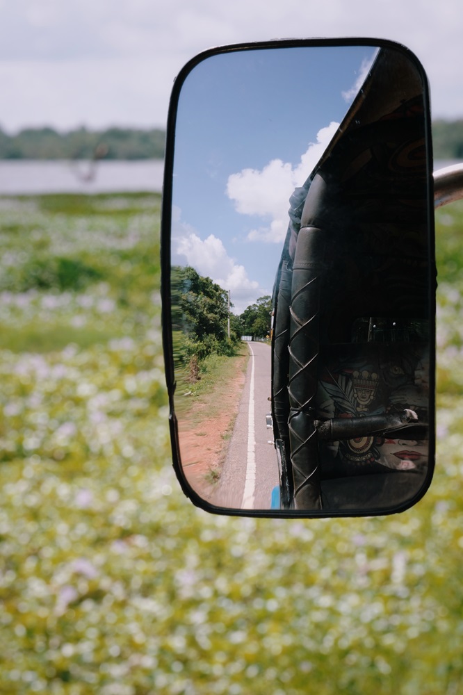 A picture of the rear view mirror of a rental tuktuk in Sri Lanka with lakeside views in the background.