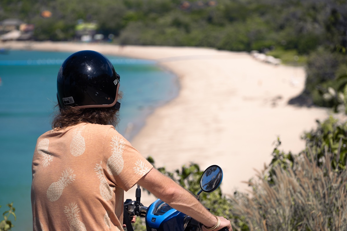 A motorcyclist on a blue scooter wearing a black helmet overlooking the curving sands of Kantiang Bay, Thailand.