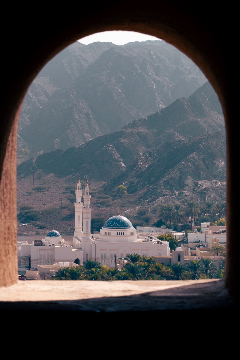 A mosque with a blue dome through the turret window of the Omani fort at Samail.