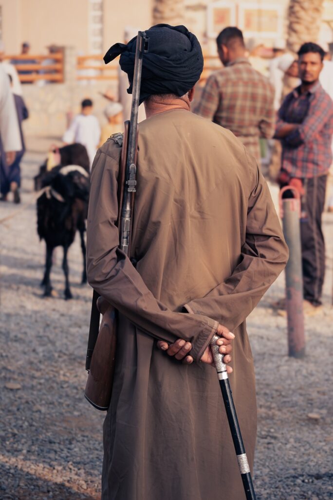 An Omani shepherd standing with his rifle and walking stick.