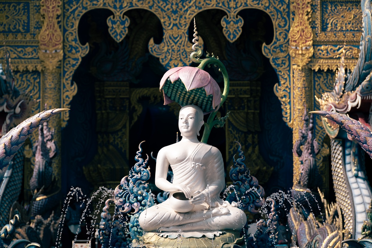 A serene looking Buddha statue sat beneath a lotus flower at one of many temples in Chiang Rai, The Blue Temple.