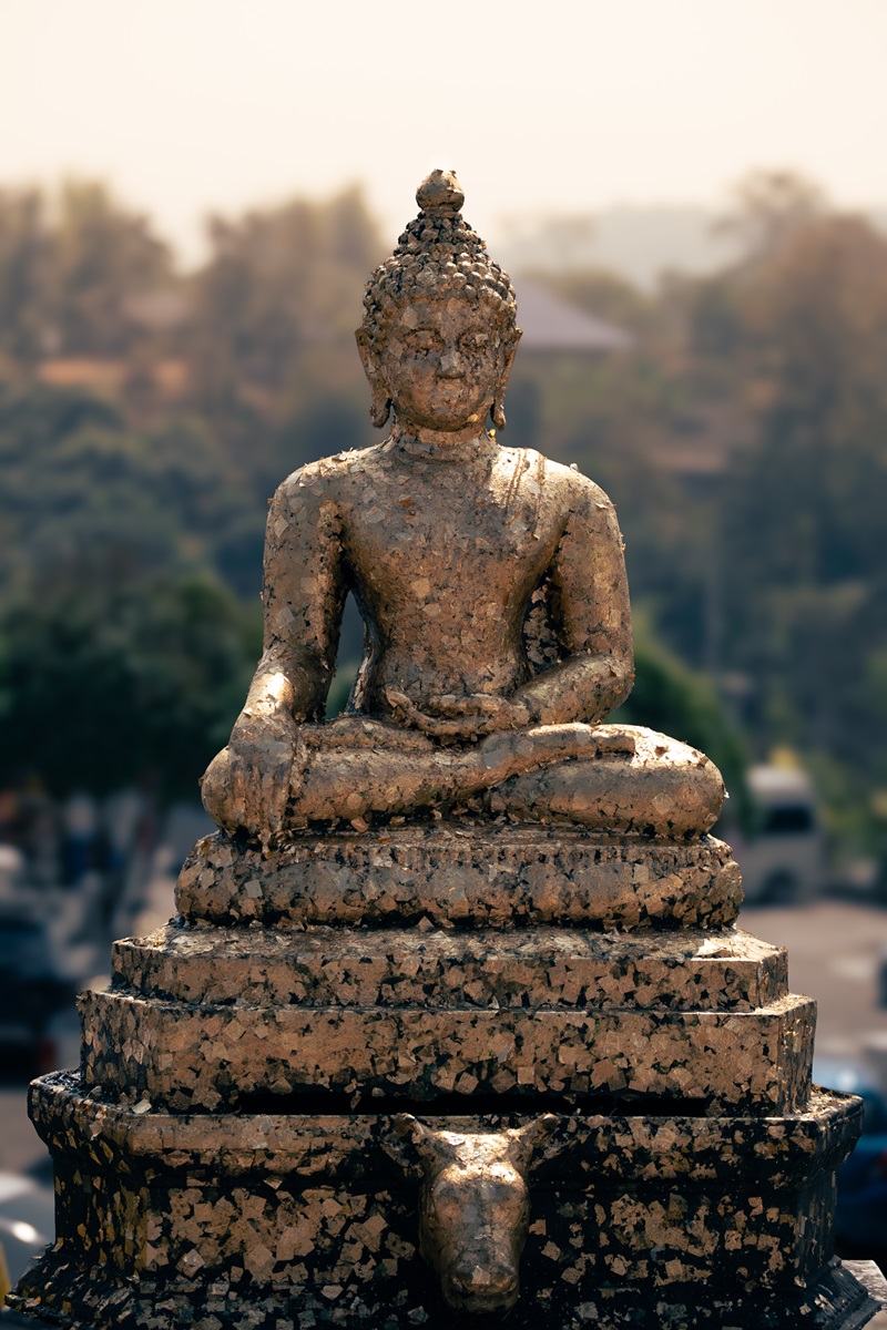 A golden Buddha made from leaf metal in a seated pose, outside the giant Goddess of Mercy statue in Chiang Rai.