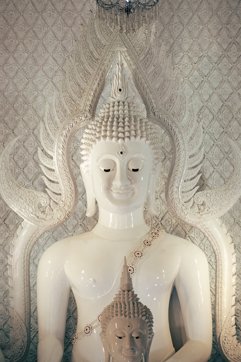 A white porcelain statue of a Buddha smiling down, with a smaller version below it.