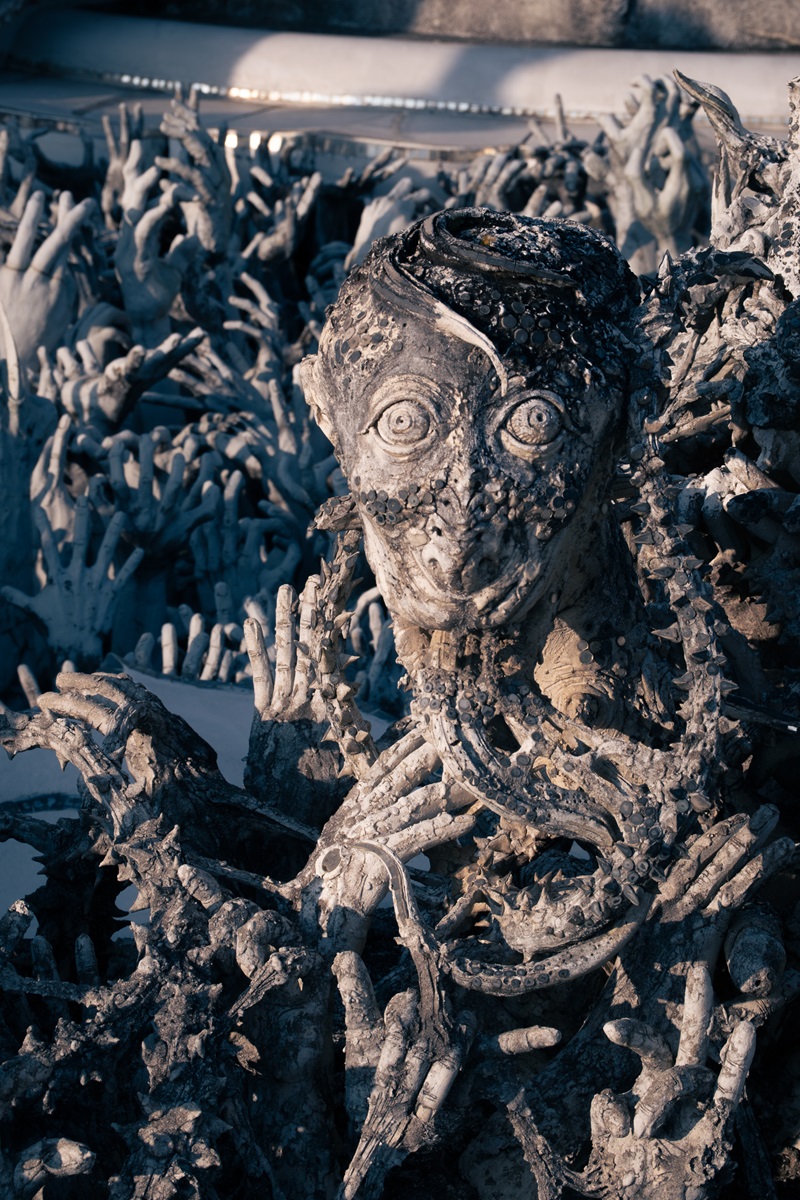 A creepy face with a long tongue nestled between outreaching hands at one of the many temples in Chiang Rai, Thailand.