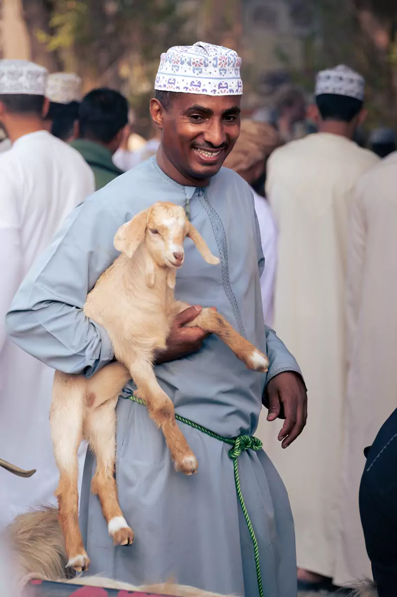 An Omani man dressed in blue, pleased with his goat purchase at the Nizwa goat market.