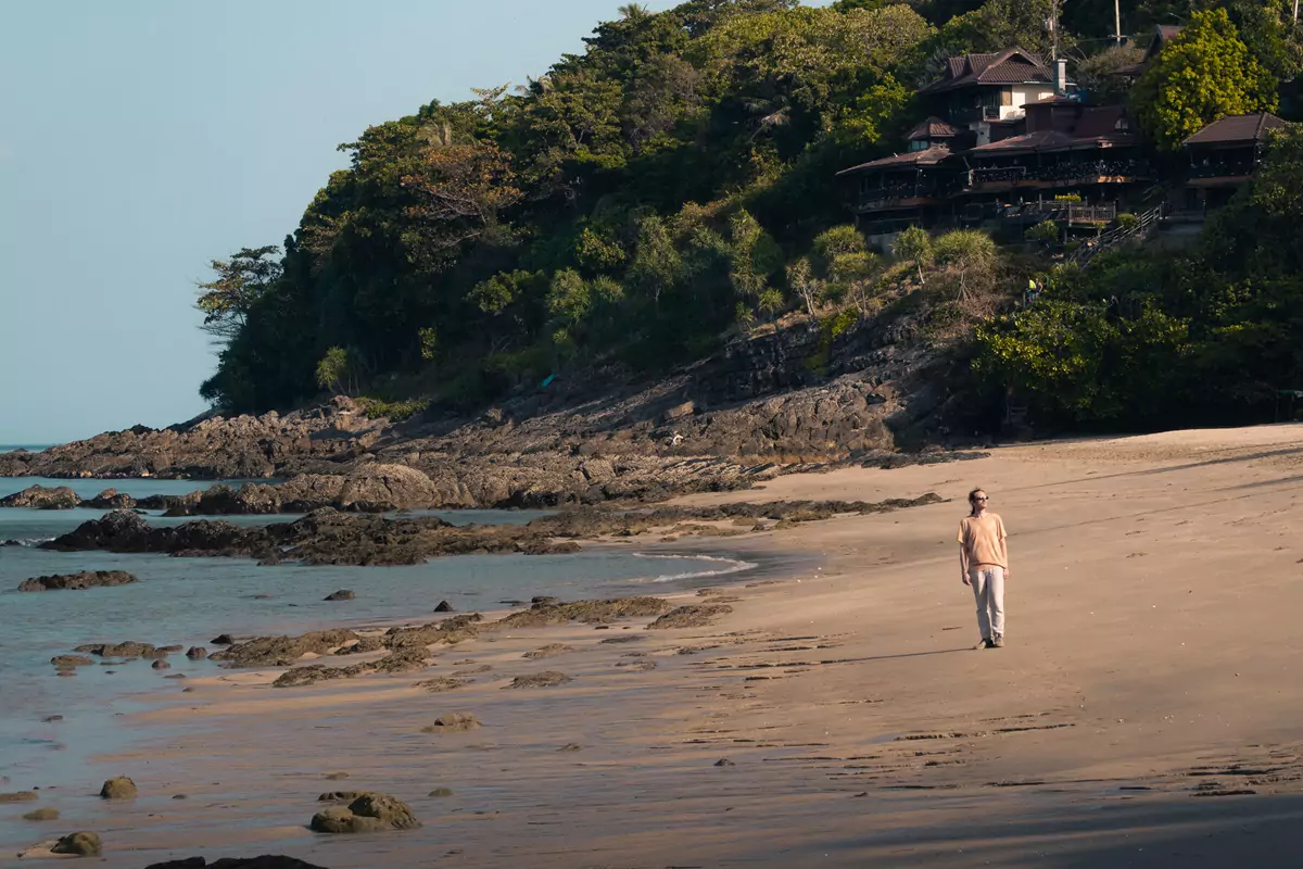 A person walking along the rocky shore of Nui Beach, Koh Chang, in the early morning.
