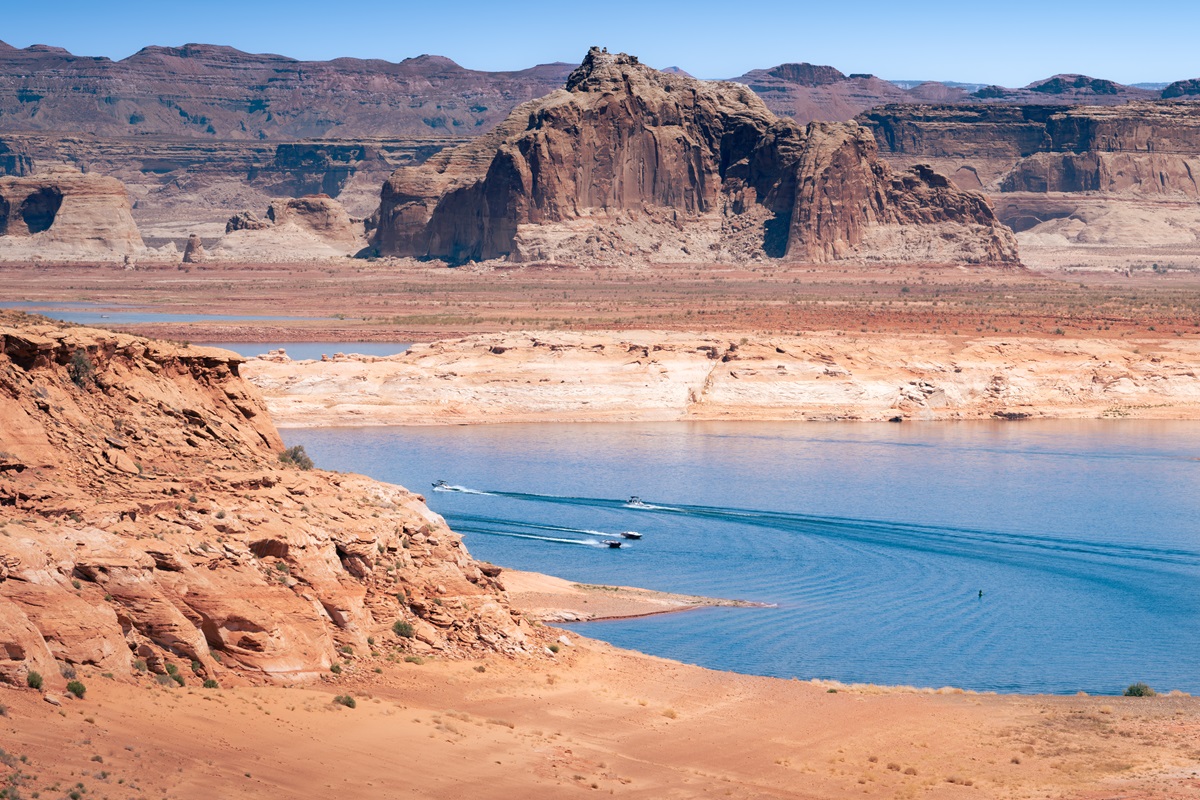 Boats in the blue waters of Lake Powell surrounded by red and white rocks formations.