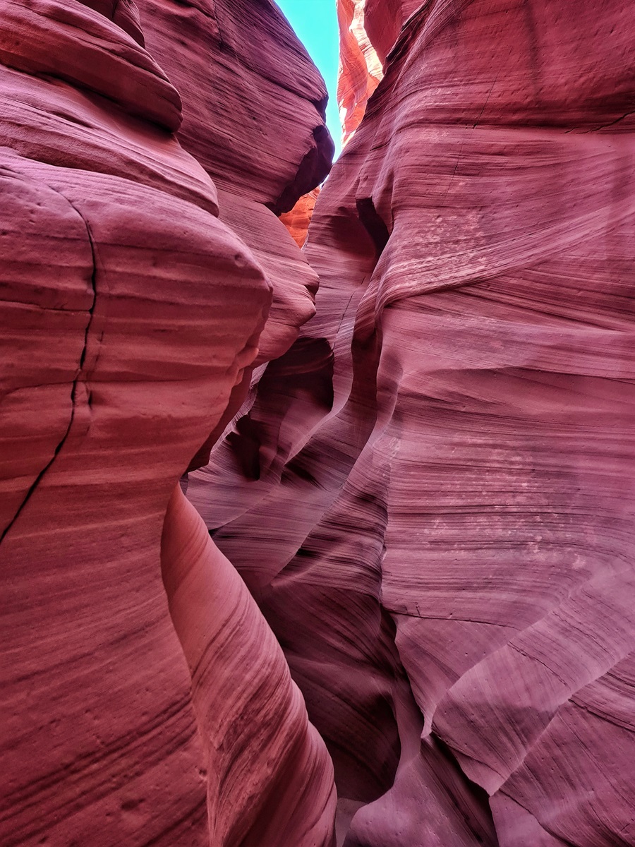 Tall, narrow passage in Canyon X with red and orange rock formations and sunlight filtering from above.