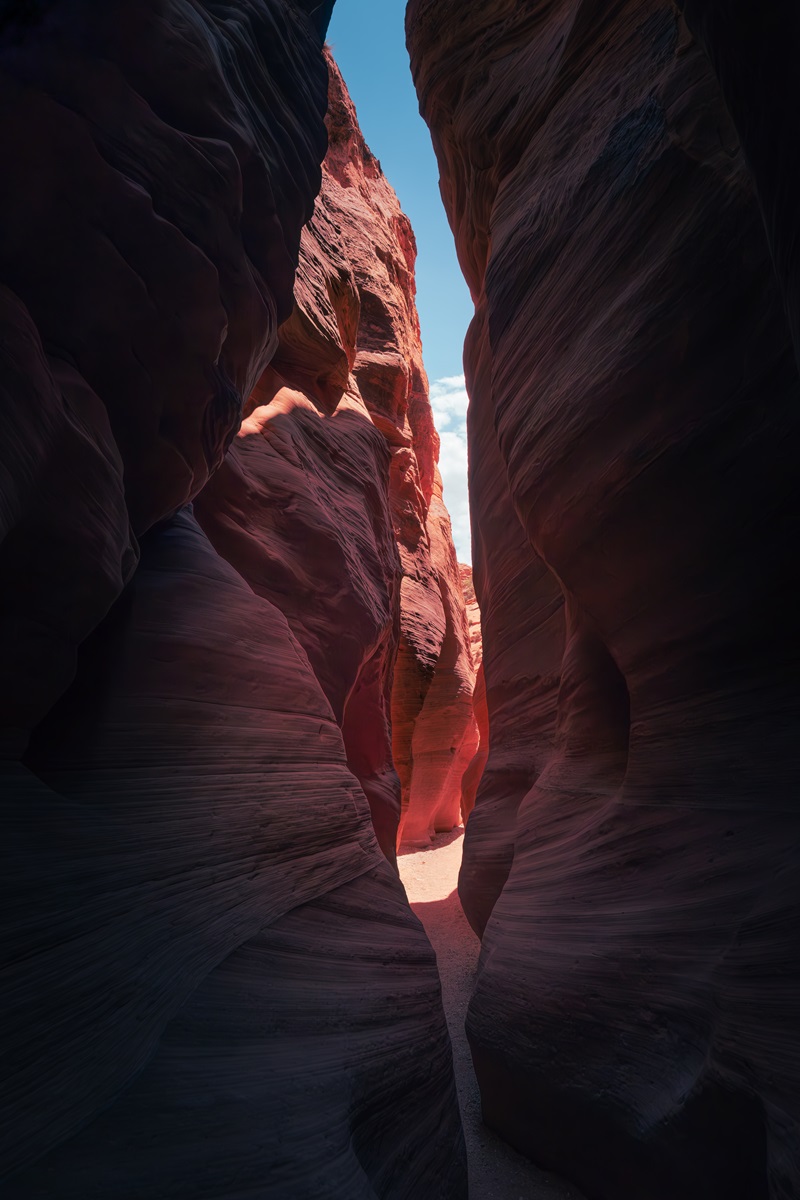 A sandy path leading through a narrow slot canyon back into the sunlit open.
