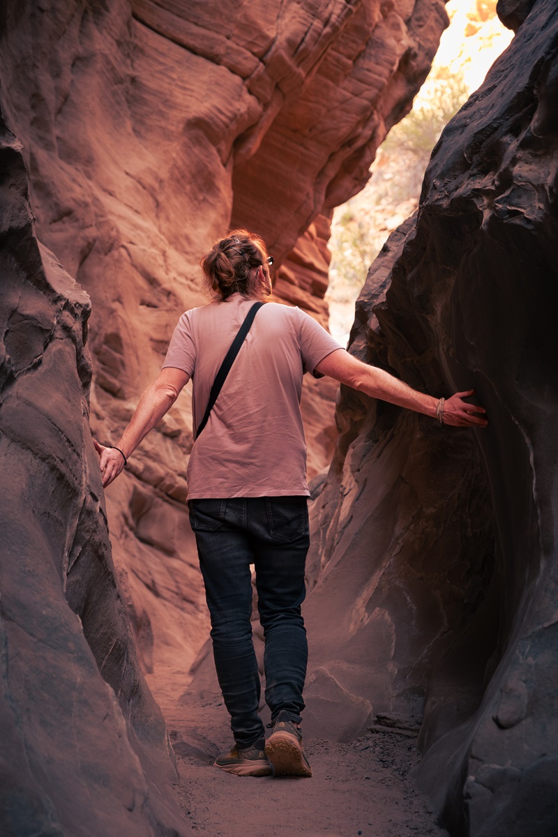 A person hiking through a slot canyon back into the open, with hands touching the narrow walls