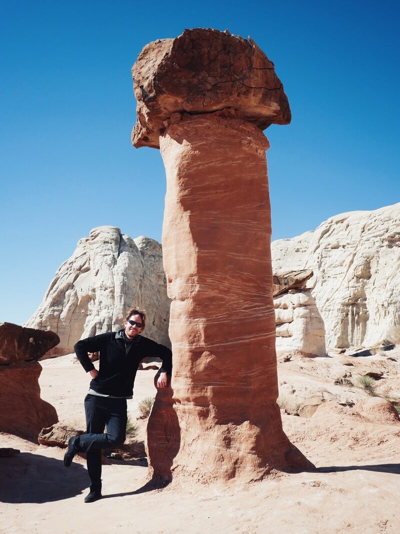 A person leaning against a giant, mushroom shaped sandstone rock formation on the Toadstool Hoodoos Trail, Utah.