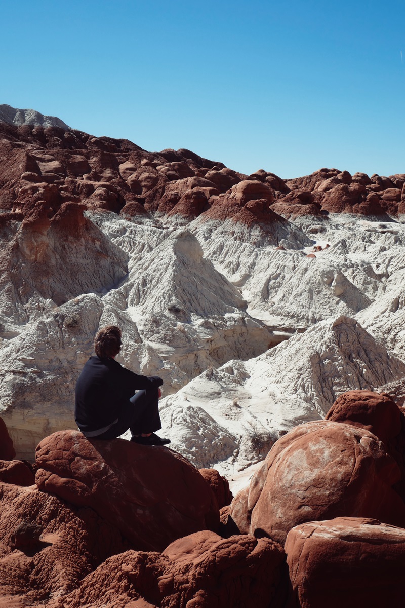 A person sat on a red sandstone boulder above a section of contrasting white sandstone at the Toadstool Hoodoos near Page.