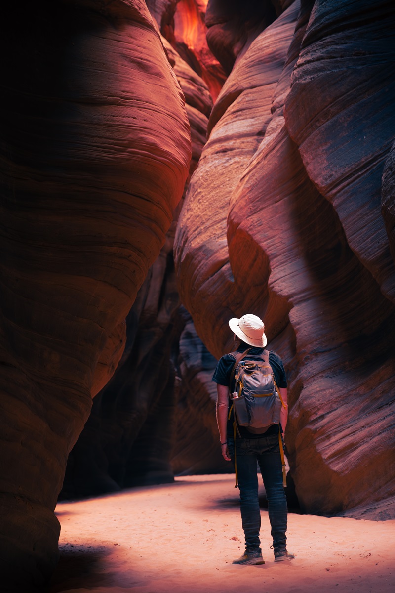 A hiker standing in soft sunlight at the base of a slot canyon.