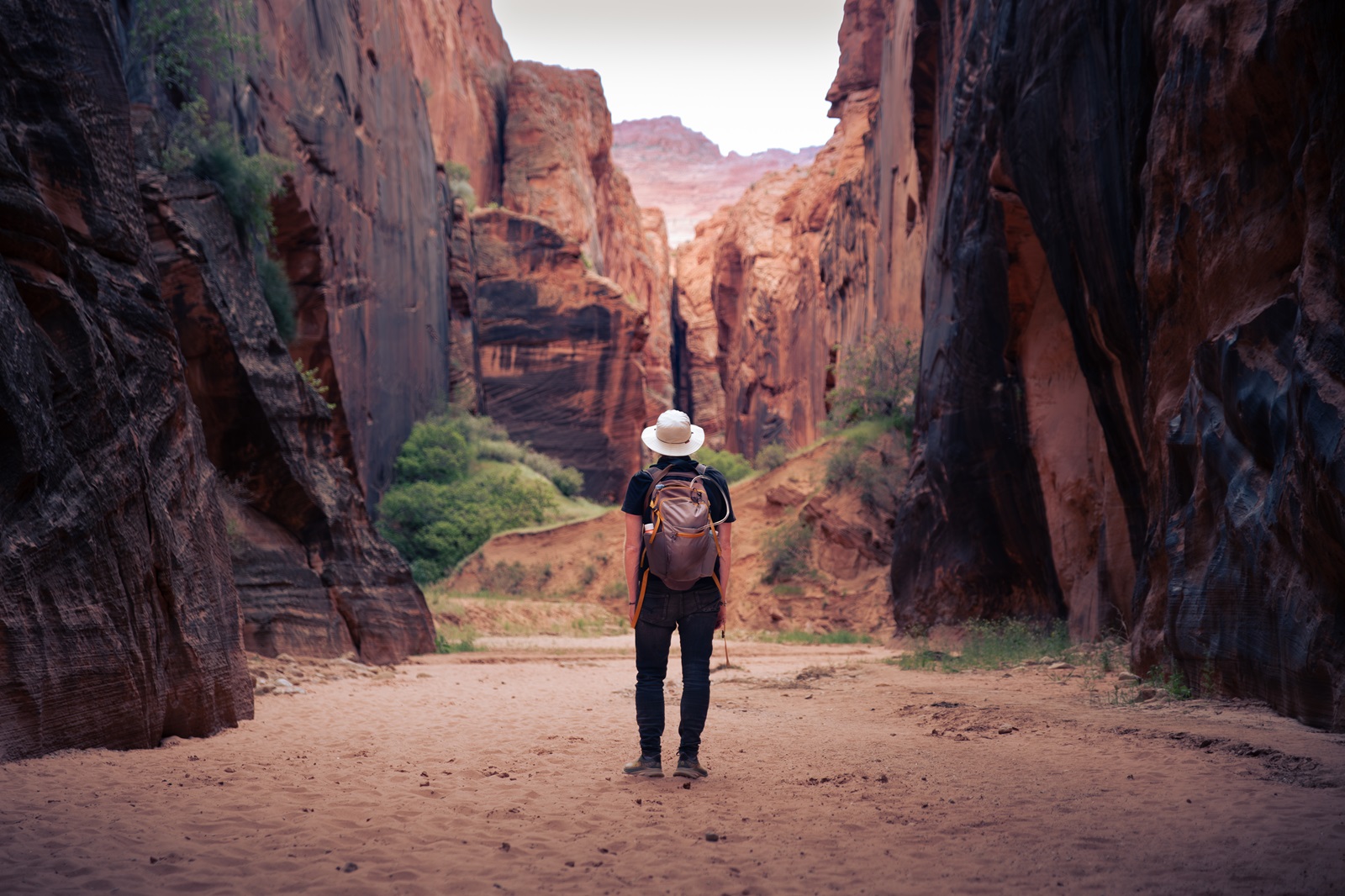 A hiker standing in an open section of Buckskin Gulch with a narrow slot canyon section in the distance.