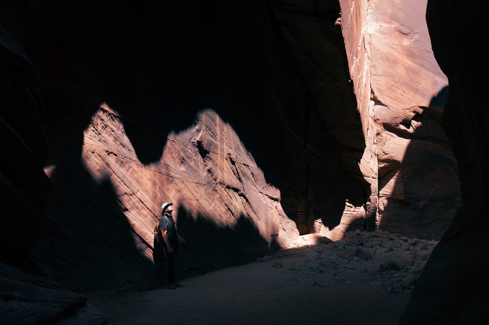A hiker leaning against the base of a cliff wall, lit up by sunlight entering through a gap above.