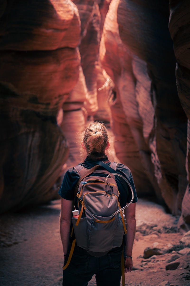 A hiker wearing a yellow and grey rucksack looking ahead into a section of slot canyon.